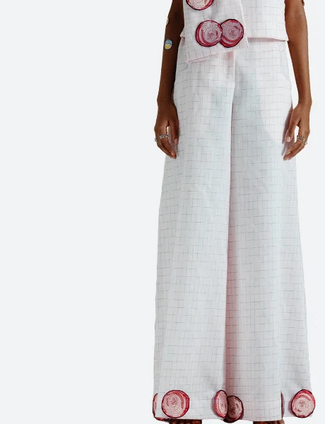 Pants category product detail view for Felix Matos featuring pale pink wide-leg pants with subtle grid texture and red circular appliqué details near the hem.