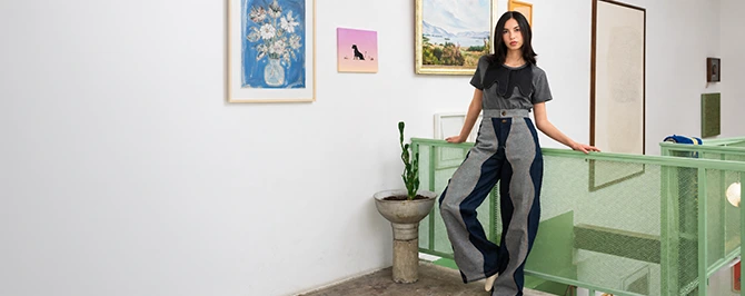 Model wearing a black and gray Felix Matos look from the Commune collection in an editorial interior setting.