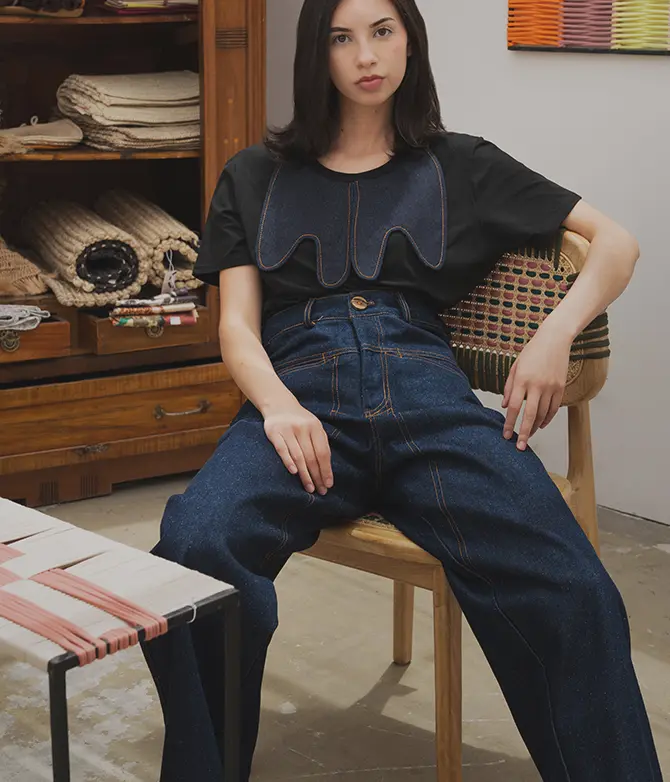 Model wearing a black top and dark denim wide-leg pants from a Felix Matos featured collection in an editorial interior setting.
